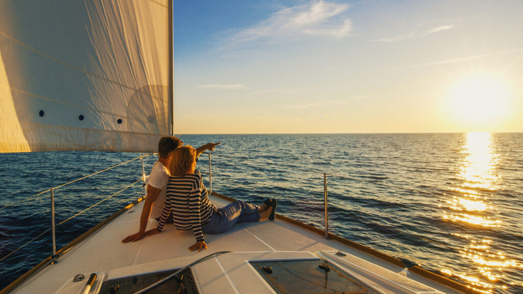 Couple sitting on prow of boat, man pointing his hand, Croatia