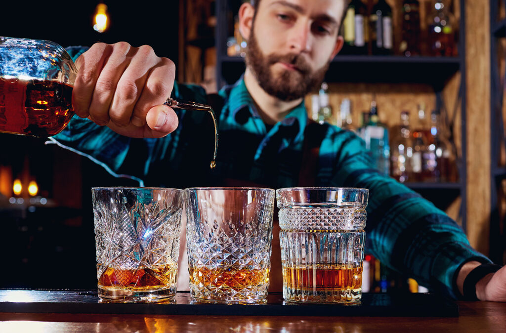 The barman pours alcohol into a glass. Close-up.