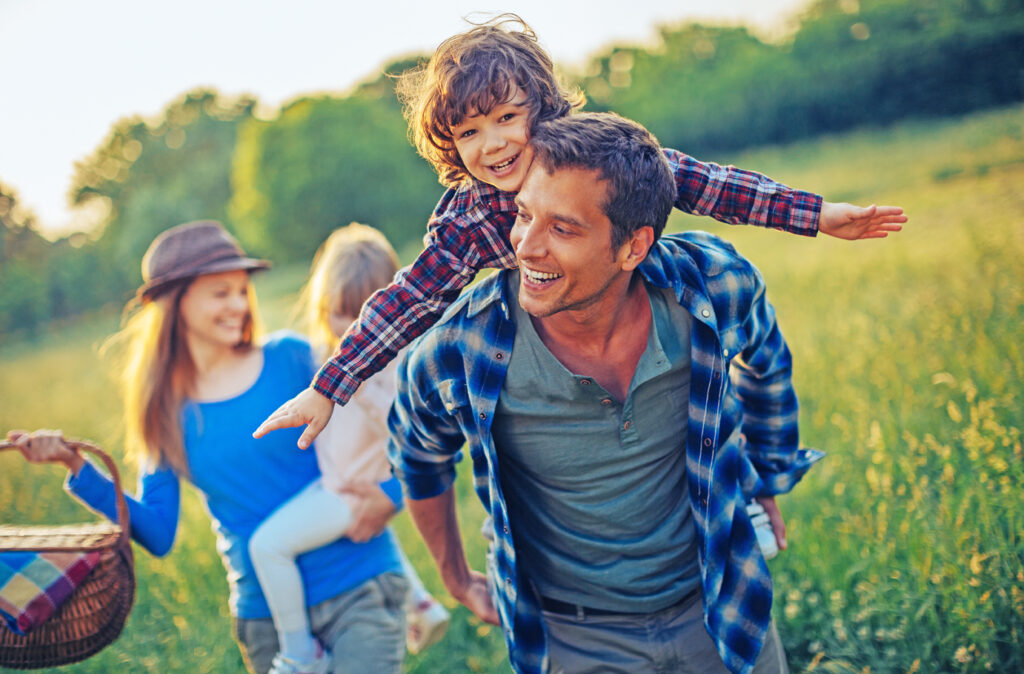 Picture of a young family going for a picnic, walking together threw high grass with the sun in their back.