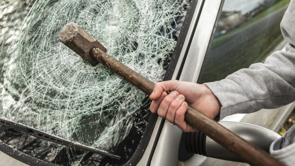 A sledge hammer embedded in a car windscreen.