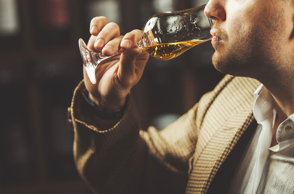 Close-up shot of sommelier tasting whiskey taste on the cellar background. Expert in the field of alcoholic beverages testing drink.