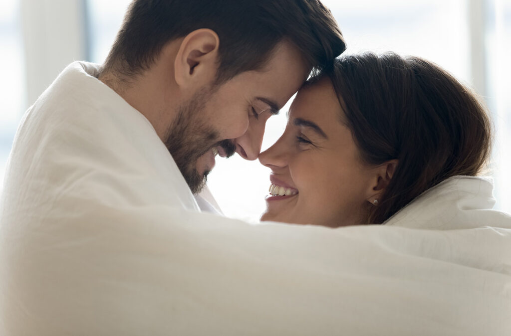 Close up profile faces happy Hispanic woman Caucasian man mixed race couple cuddling touch foreheads covered in warm blanket enjoy romantic weekend. Hotel and tourists newly-weds, heat system concept