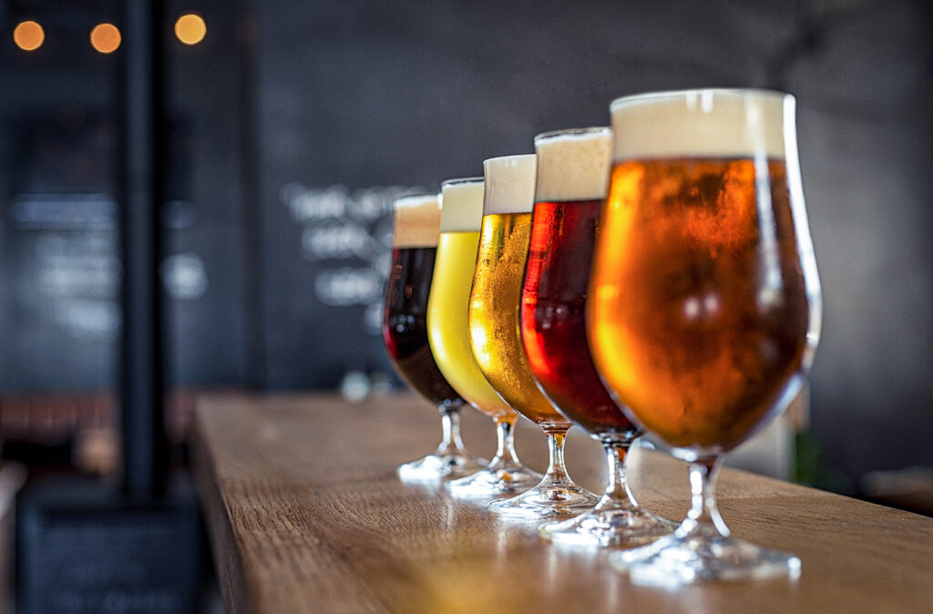 Glasses with different sorts of craft beer on wooden bar. Tap beer in pint glasses arranged in a row. Closeup of five glasses of different types of draught beer in a pub.