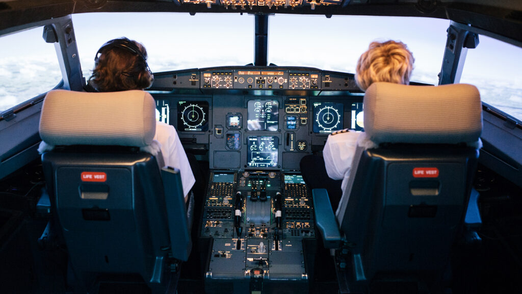 A pilot and a trainee co-pilot sitting the cockpit of a flight simulator during a training session.