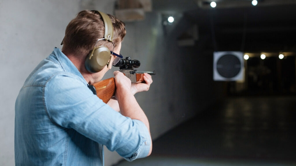 Hitting the bulls eye. Handsome confident serious man holding the rifle and looking into the target while trying to hit the bulls eye