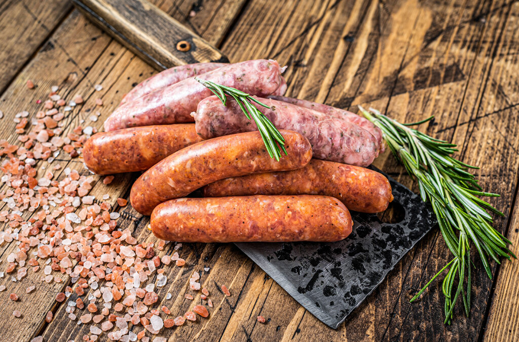 Assorted Raw pork and beef sausages on a butcher meat cleaver. wooden background. Top View.