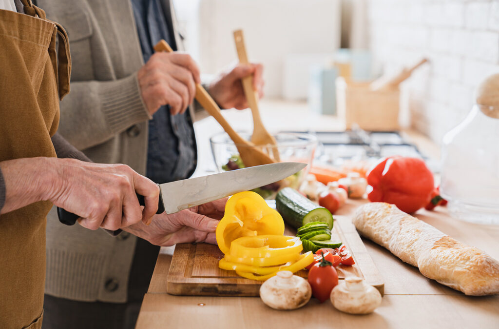 Closeup cropped focused image of old senior elderly couple grandparents family spouses cooking together, cutting vegetables at home kitchen, making vegan vegetarian salad