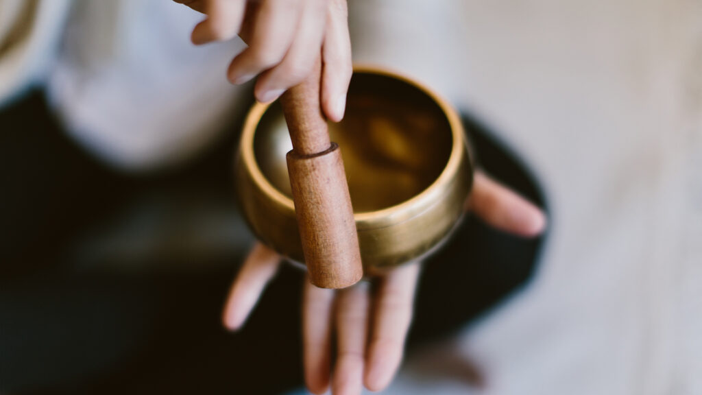 An angle shot of a woman using a Tibetan meditation singing bowl.