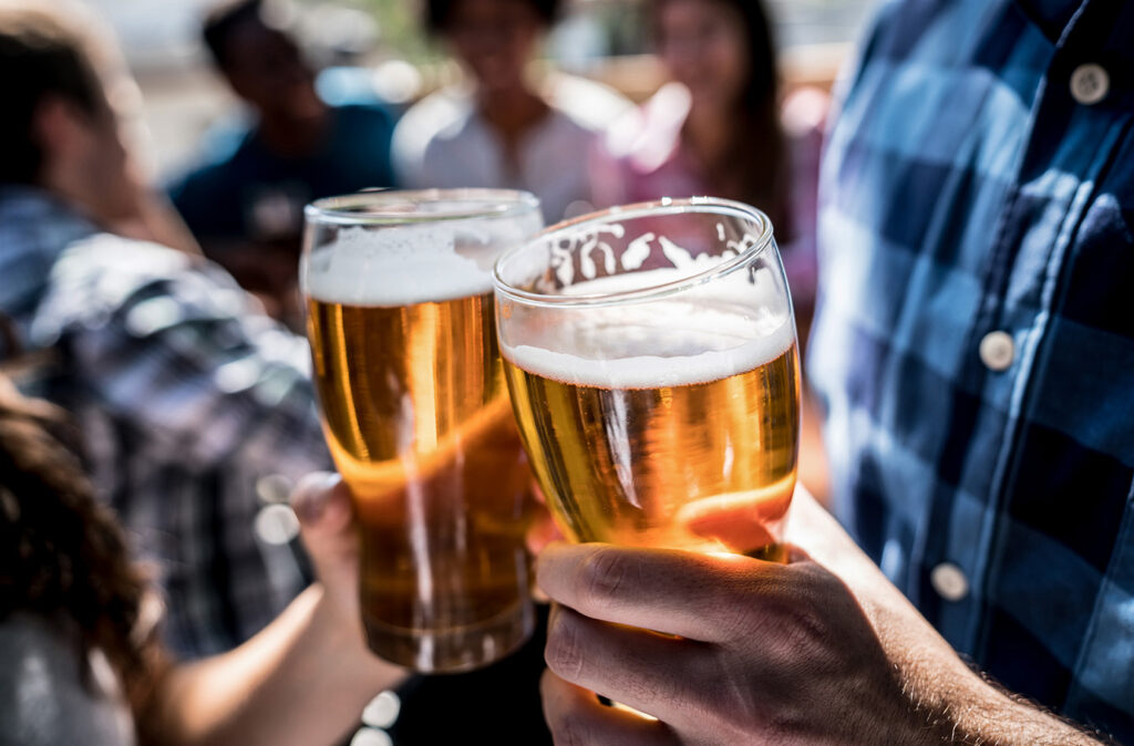 Close up of a customers at a bar holding a beer and making a toast with people having fun at the background