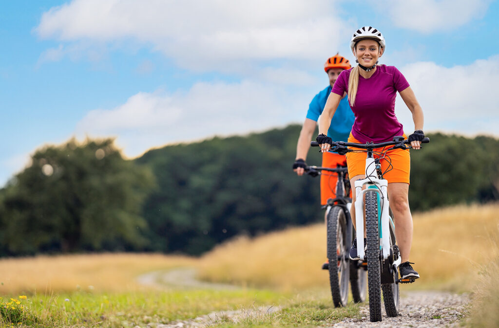 happy smiling couple cycling down gravel road in rural landscape with elctric mountain bikes in summer, focus on woman, place for text