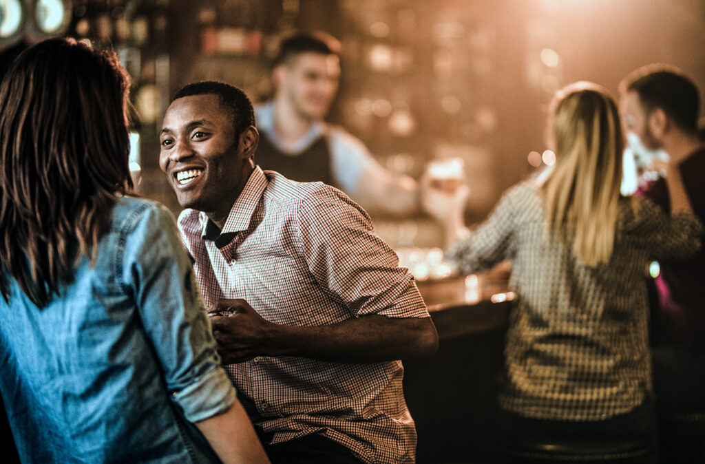 Happy black man enjoying in a talk with his girlfriend while being in a bar. There are people in the background.