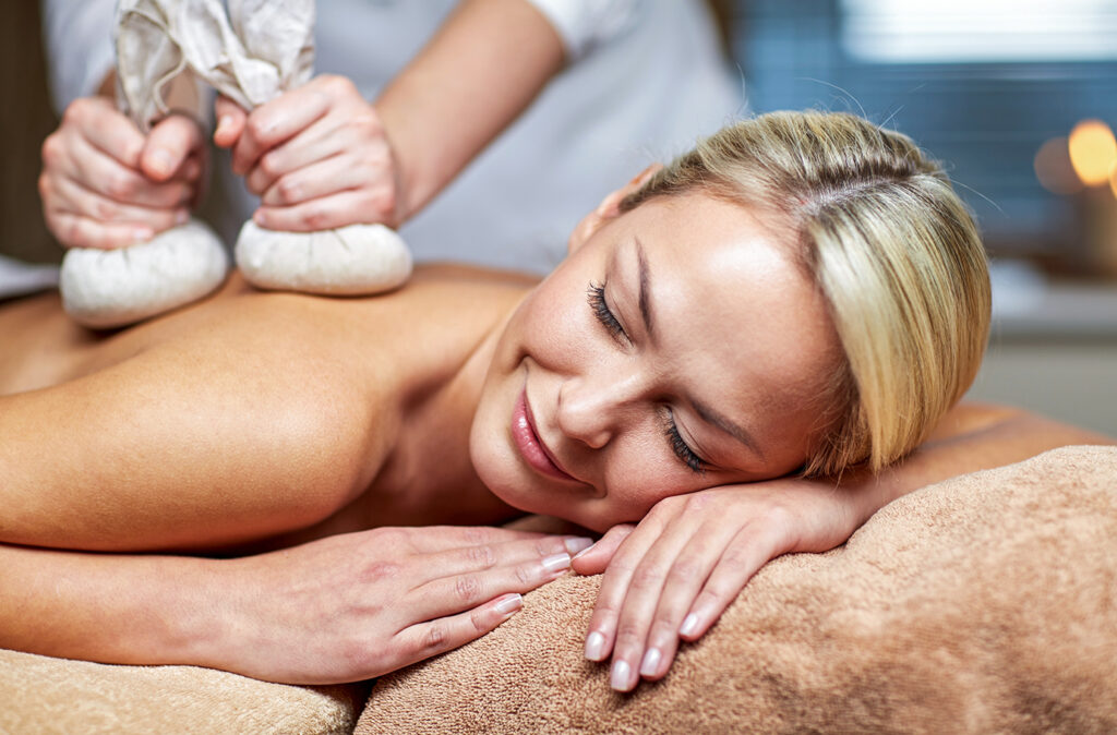 people, beauty, spa, healthy lifestyle and relaxation concept - close up of beautiful young woman lying and having herbal bag massage in spa