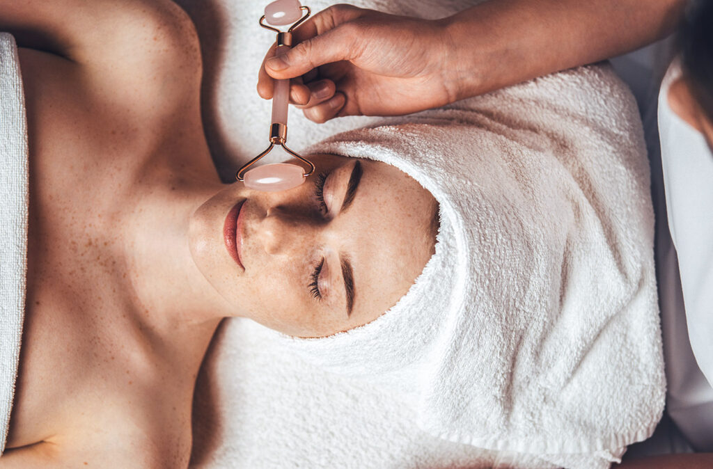 Close up portrait of beautician's hand massaging patient's face with jade roller at spa salon. Beauty woman face skin care. Body care, spa.