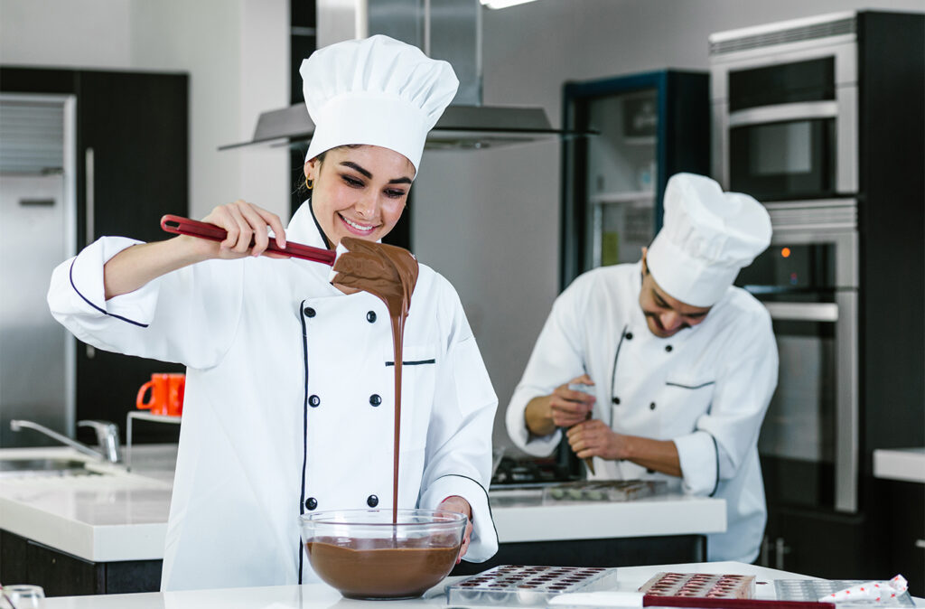 young latin couple woman and man chocolatier in chef uniform and hat preparing mexican chocolates bonbon candies at kitchen in Mexico Latin America