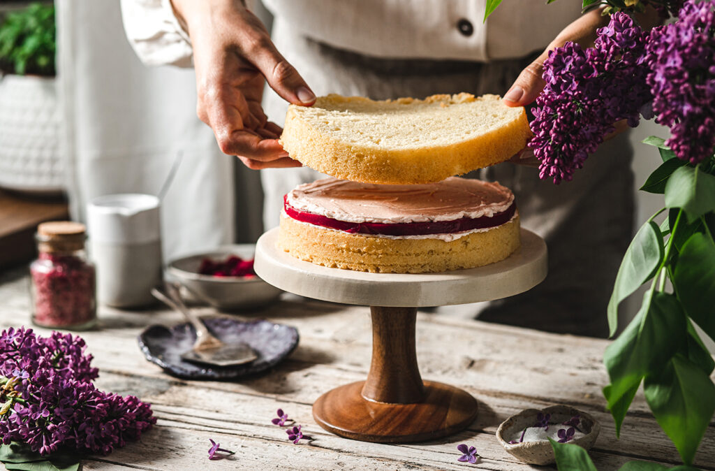 Close-up of female chef preparing cake. Woman making a layer cake with ingredients on table.