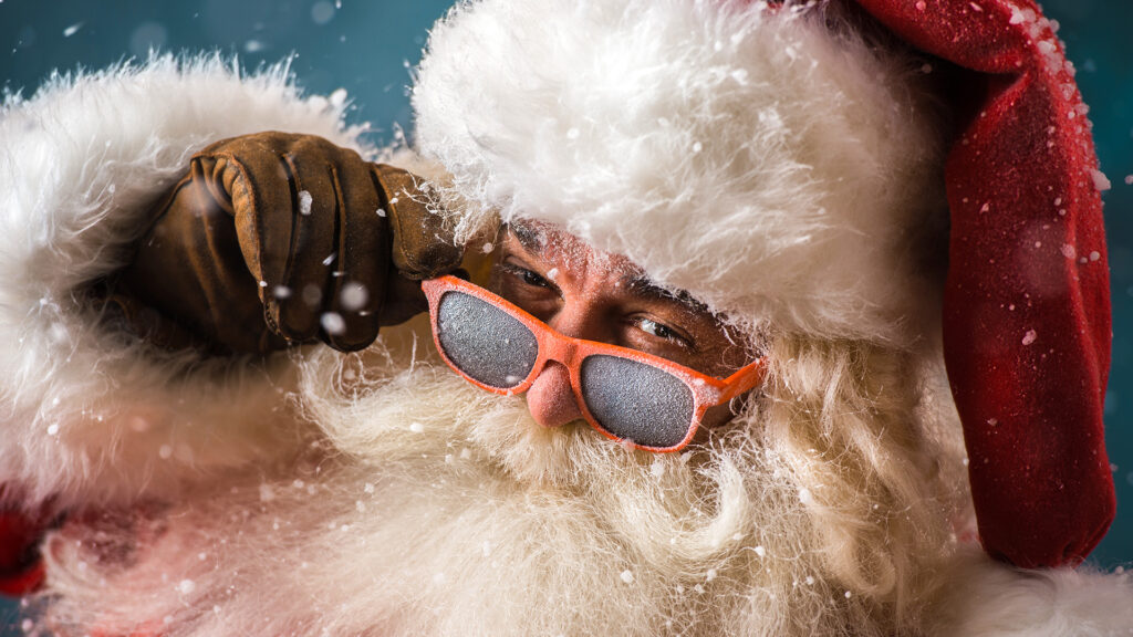 Santa Claus wearing sunglasses dancing outdoors at North Pole in snowfall. He is celebrating Christmas after hard work