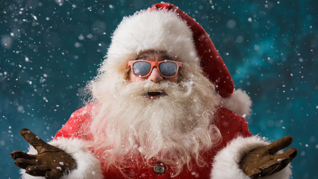 Santa Claus wearing sunglasses dancing outdoors at North Pole in snowfall. He is celebrating Christmas after hard work