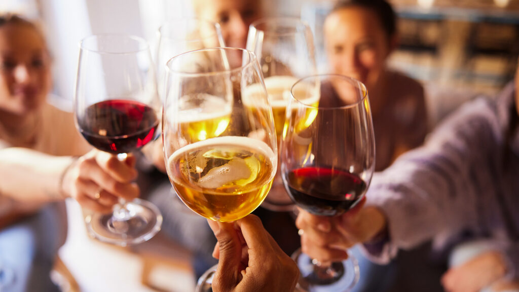 Close-up of wine and beer cups. Incidental people are making a toast.