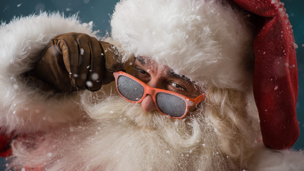 Santa Claus wearing sunglasses dancing outdoors at North Pole in snowfall. He is celebrating Christmas after hard work