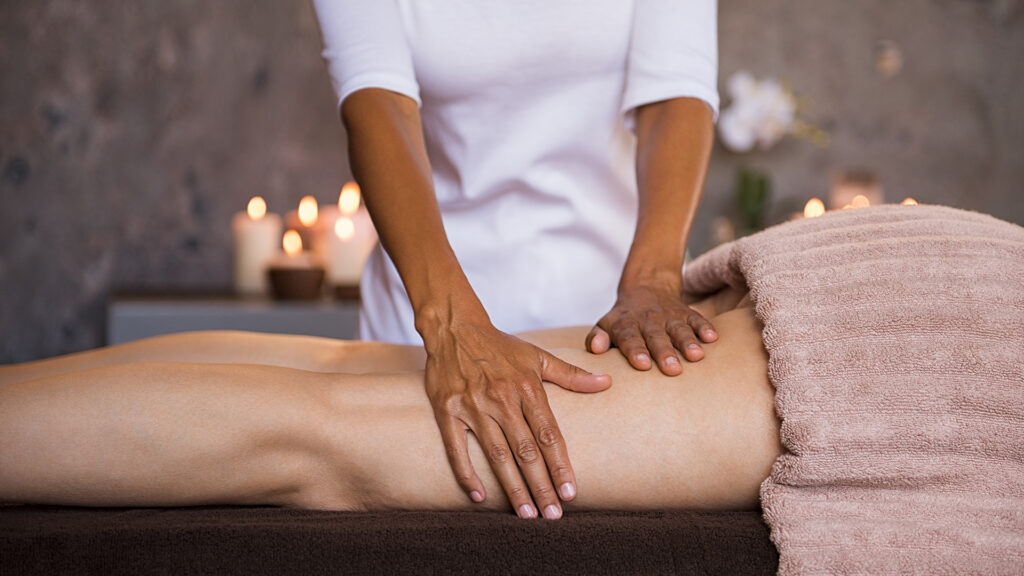 Therapeutic massage for senior woman by beautician at spa salon. Closeup of professional masseuse hands massaging woman legs at wellness center. Anti cellulite treatment and leg drainage on mature woman.