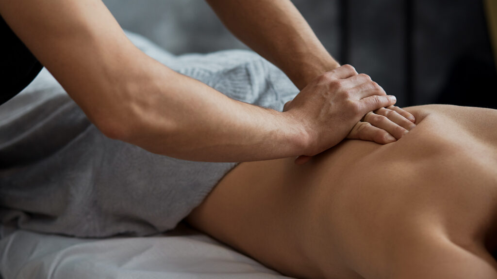 Young handsome man enjoying a back massage. Professional massage therapist is treating a male patient in apartment. Relaxation, beauty, body and face treatment concept. Home massage.