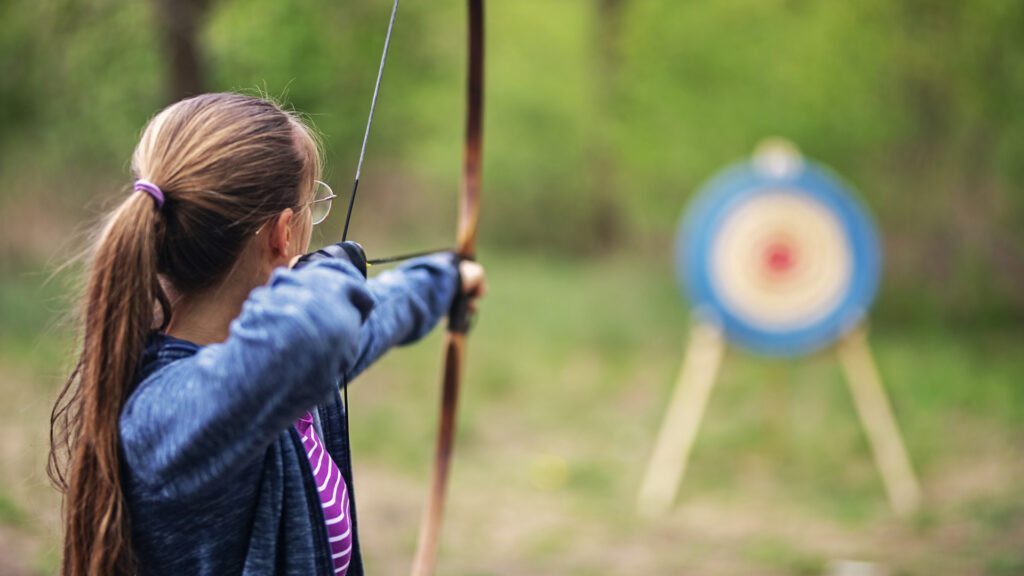 Teenage girl shooting bow outdoors on spring day.
Nikon D850