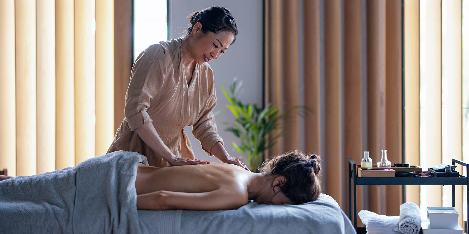 Beautiful Asian Female Massage Therapist Giving a Massage to a Woman Lying Face Down Beautiful Asian female masseuse giving a massage to a woman lying face down on the bed. They are in a spa center or a massage parlour.