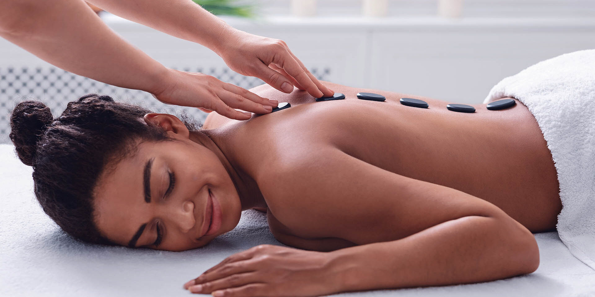Therapist hands and young african lady enjoying hot stones massage Therapist hands and young african woman enjoying hot stones massage, spa day concept