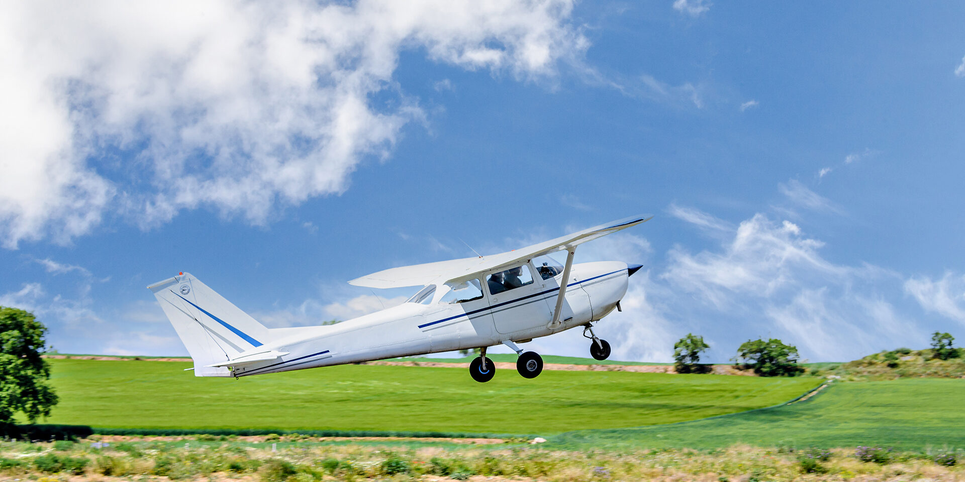 Single engine ultralight airplane taking off from airfield under blue sky with white clouds
