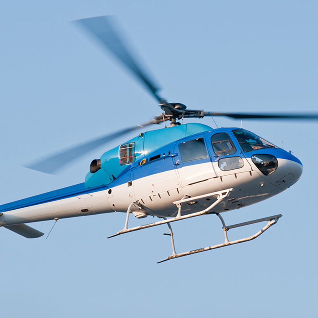 A helicopter two-tone colored (blue and white) is flying in the sky in Yokohama, Japan. Low angle view of the fuselage soring high into the sky.