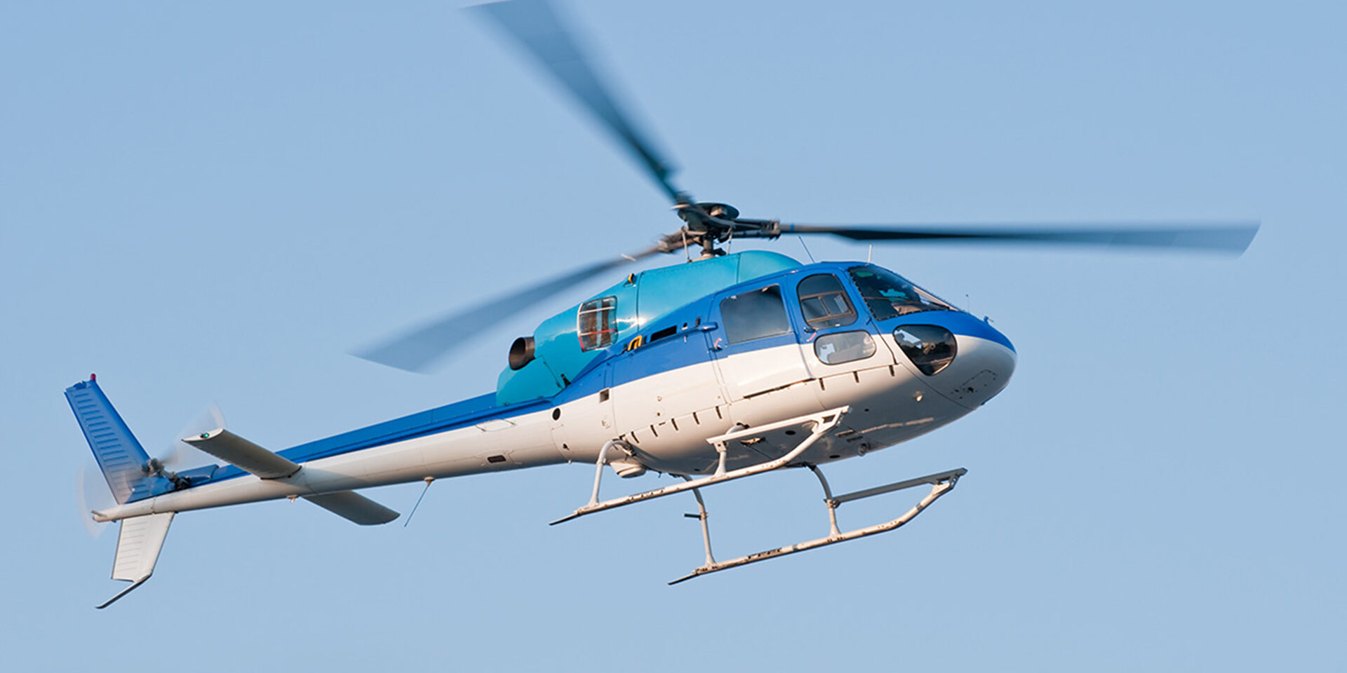 Helicopter in flight against blue sky A helicopter two-tone colored (blue and white) is flying in the sky in Yokohama, Japan. Low angle view of the fuselage soring high into the sky.