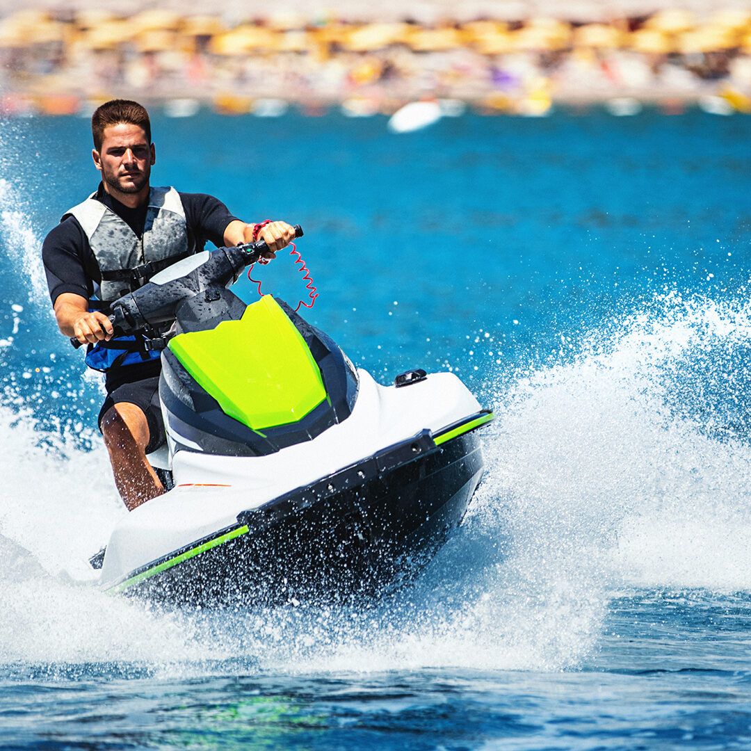 Closeup front view of a young man riding a jet ski on a sunny summer day at open sea. He's wearing swimming suit and a life jacket.