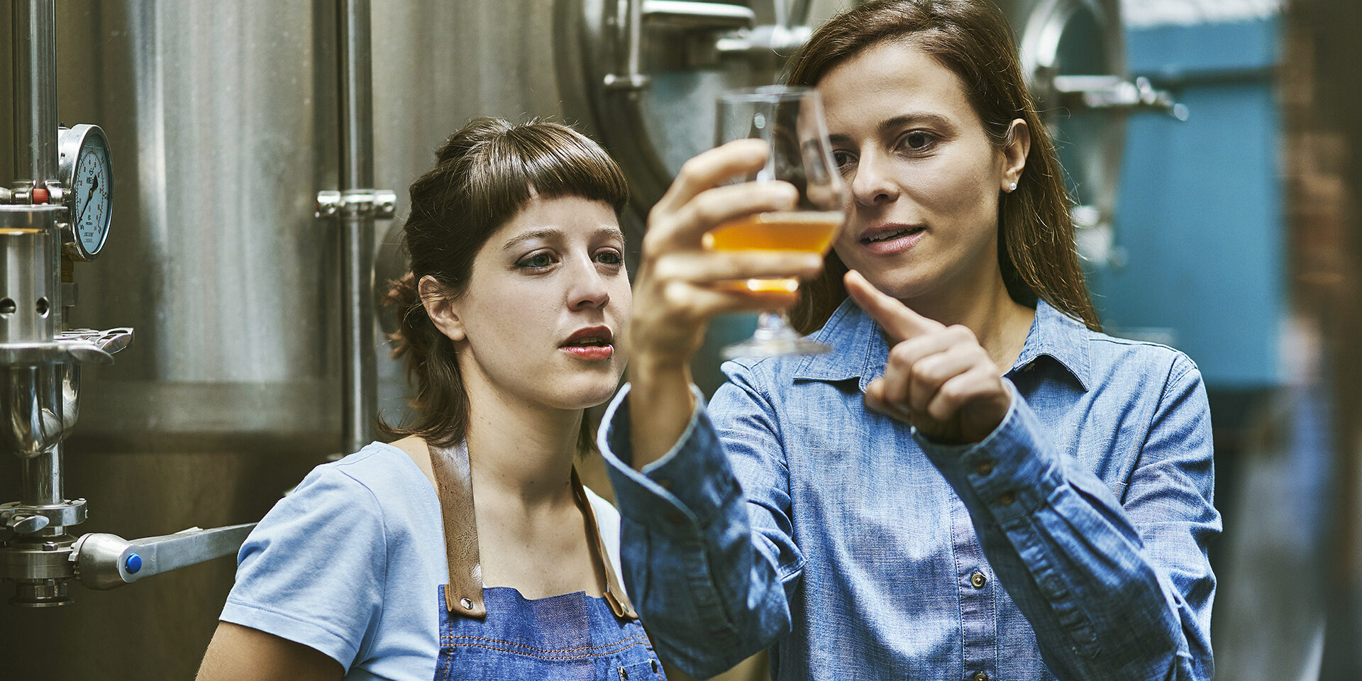 Close-up of Hispanic women in mid 30s working in craft beer brewery and checking sample for quality.