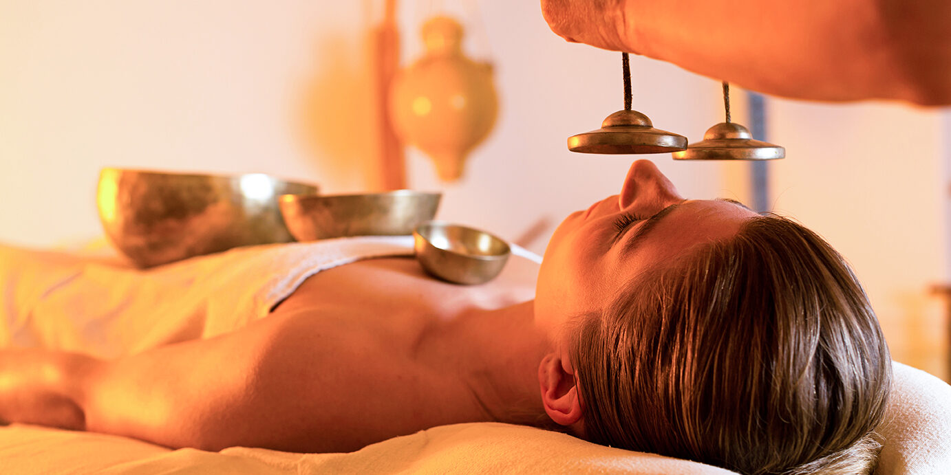 Woman in wellness and spa setting having a singing bowl massage therapy, the therapist is waking her up with cymbals