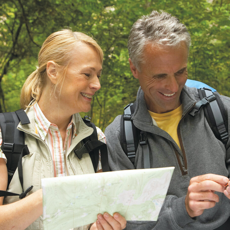 Mature man and woman looking at map and using GPS in forest