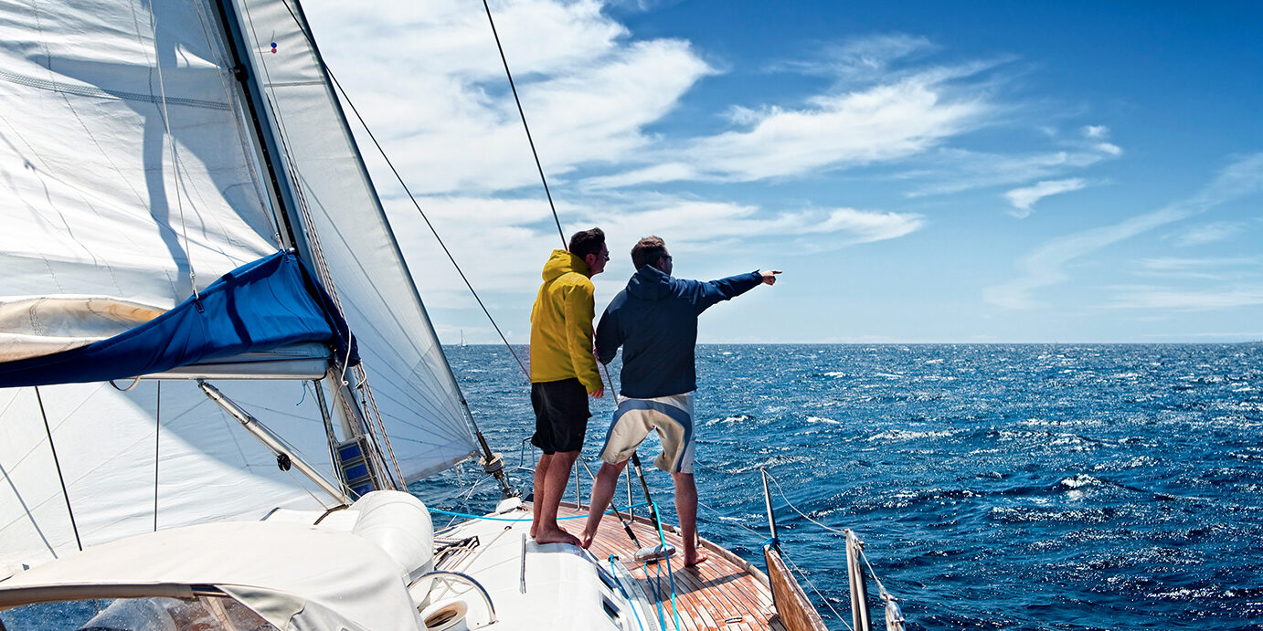 Sailing crew members on sailing ship observing the sea.