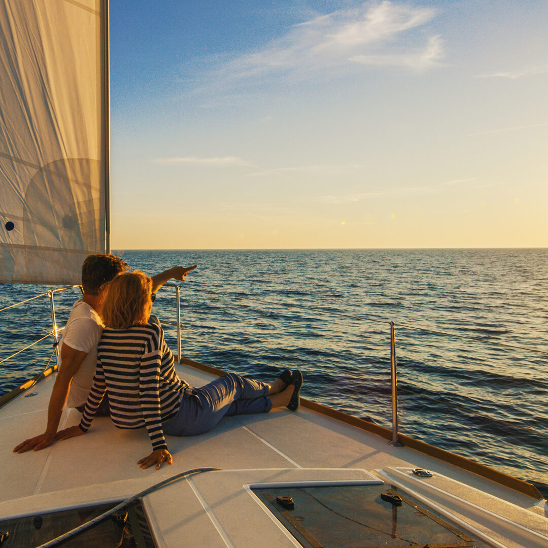 Couple sitting on prow of boat, man pointing his hand, Croatia