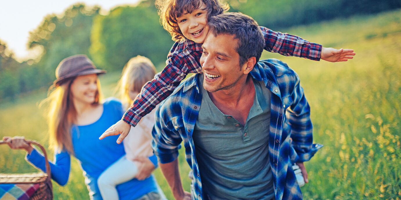 Picture of a young family going for a picnic, walking together threw high grass with the sun in their back.