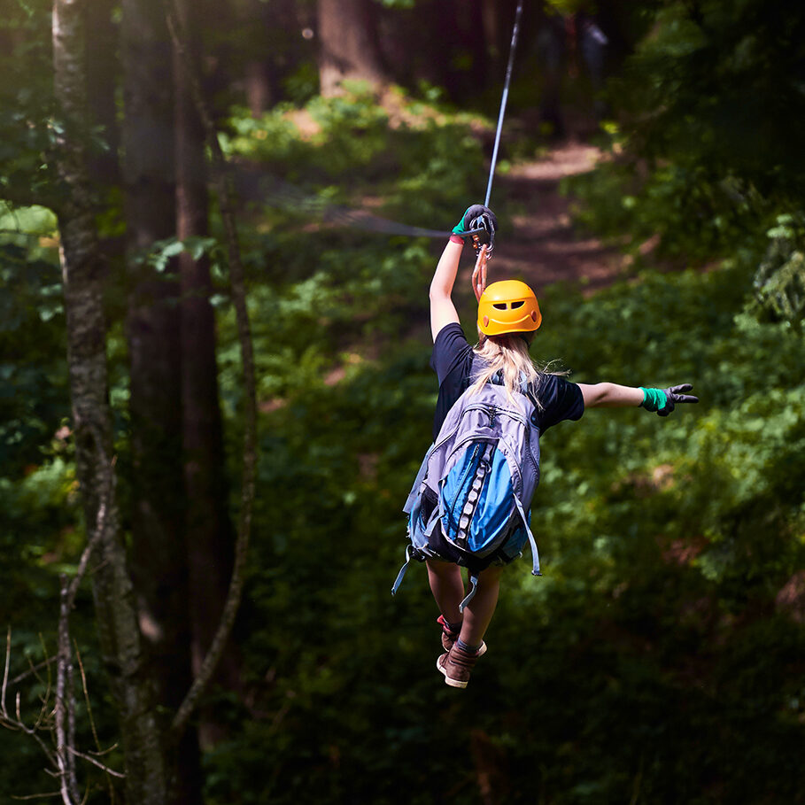 rear view of woman in the forest with her backpacker enjoying adventure on tyrolean traverse.