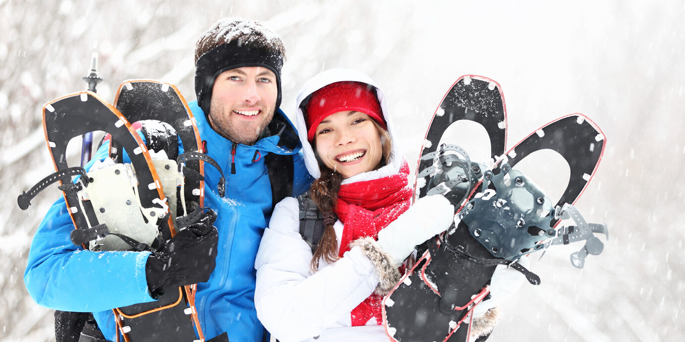 Winter couple outdoors on snowshoes Winter couple happy outdoor hiking in snow on snowshoes. Healthy lifestyle photo of young smiling active mixed race couple snowshoeing outdoors. Asian woman, caucasian man.