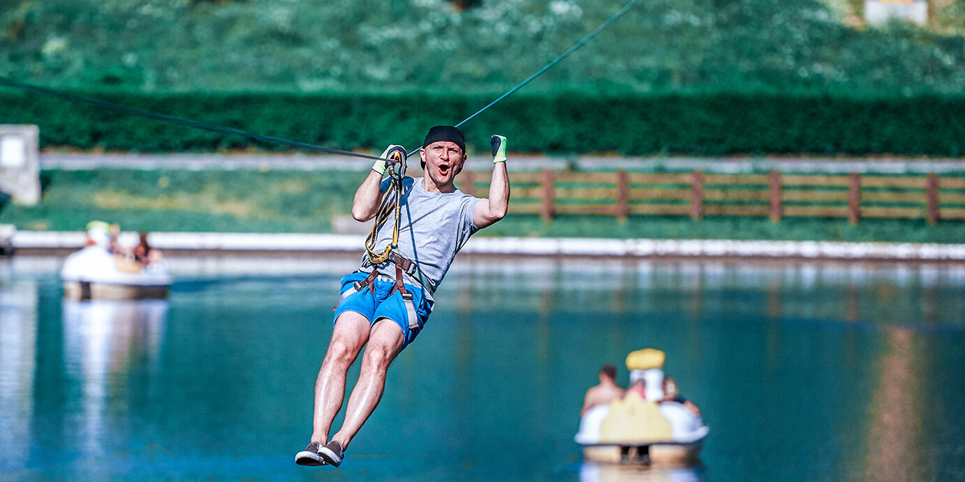 cheerful and energic man zip lining over the lake in summer day, adventure time.looking at camera.