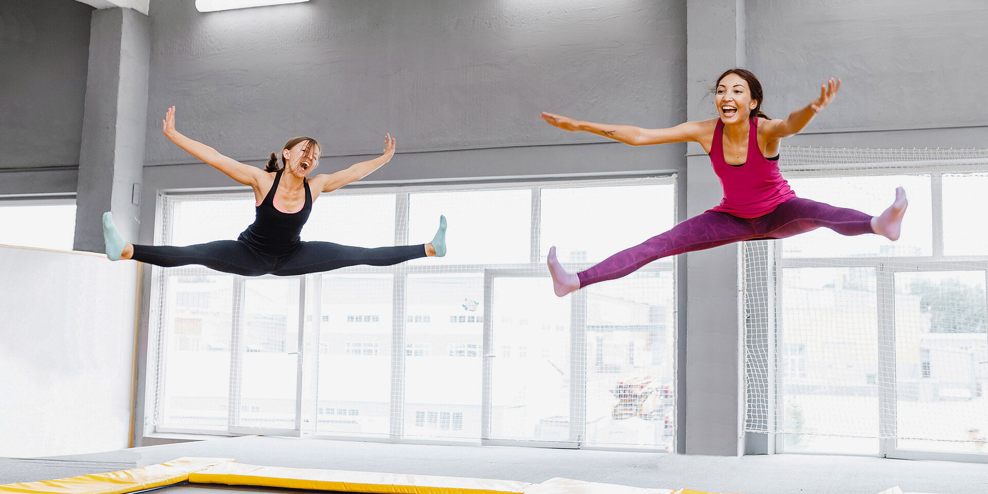 Two young woman friends jumping on a trampoline and doing split indoors Two young woman friends jumping on a trampoline and doing split indoors
