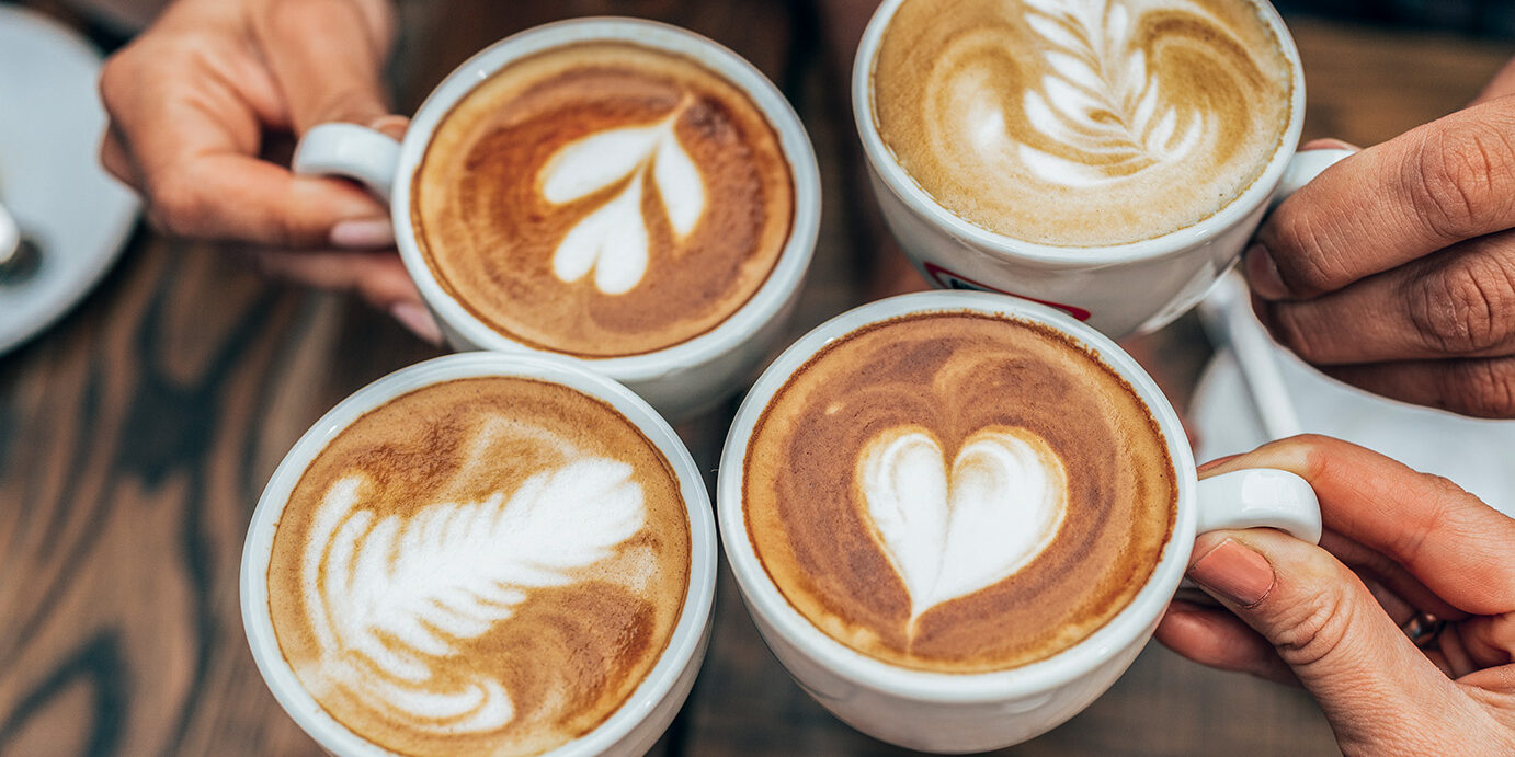 People hands holding cups of cappuccino. Friends drinking coffee together. Hands holding modern looking cups of cappuccino. Tasty and good looking coffee.