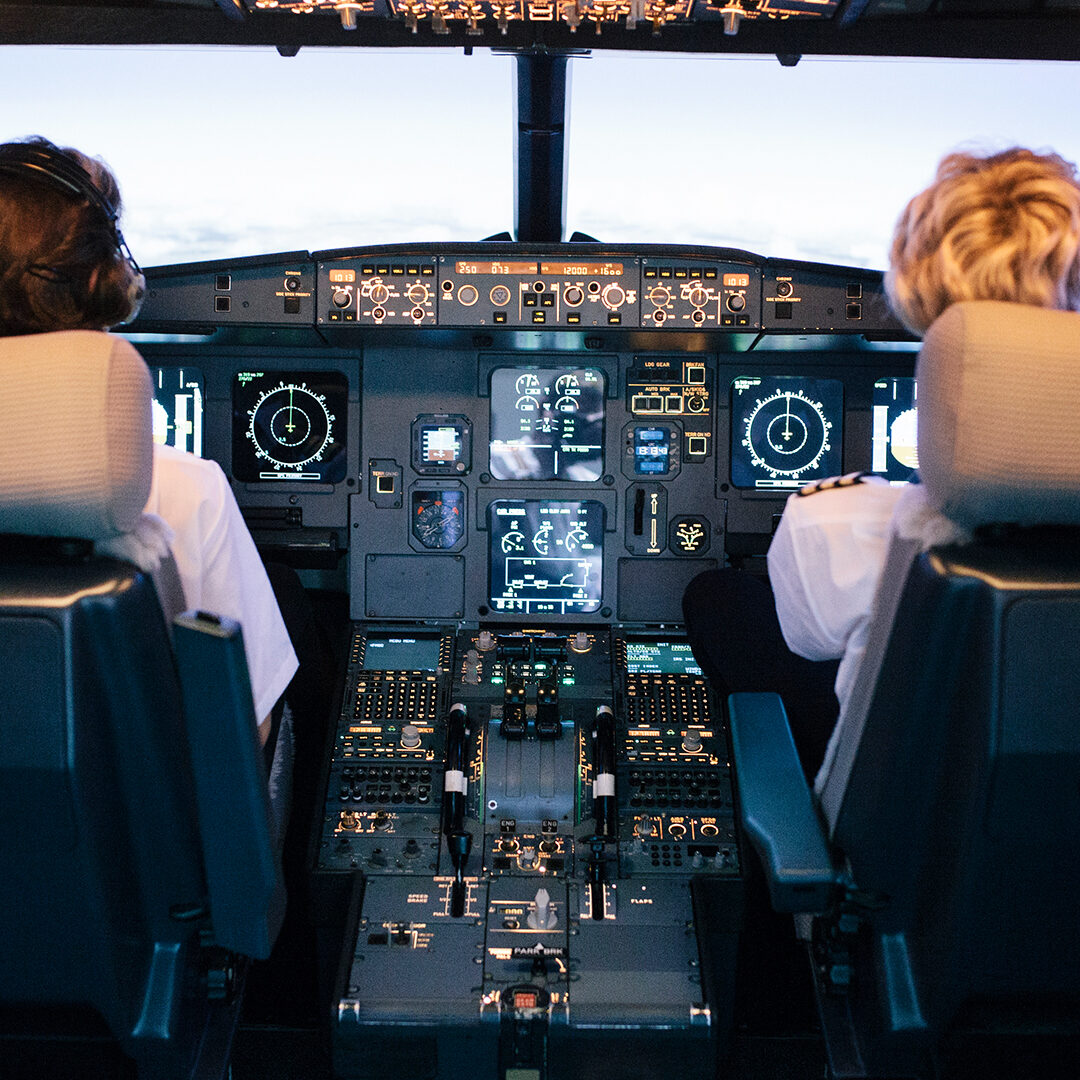 A pilot and a trainee co-pilot sitting the cockpit of a flight simulator during a training session.