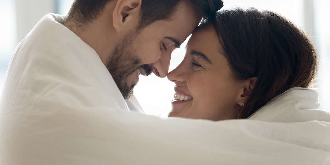 Close up profile faces happy Hispanic woman Caucasian man mixed race couple cuddling touch foreheads covered in warm blanket enjoy romantic weekend. Hotel and tourists newly-weds, heat system concept