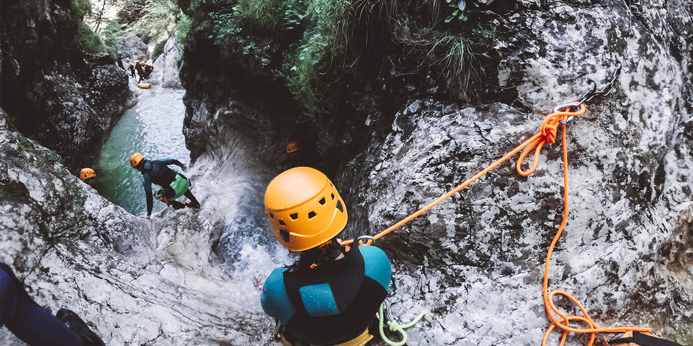 Woman canyoning in Slovenia, woman wearing neoprene and safety gear rappelling in the canyon.