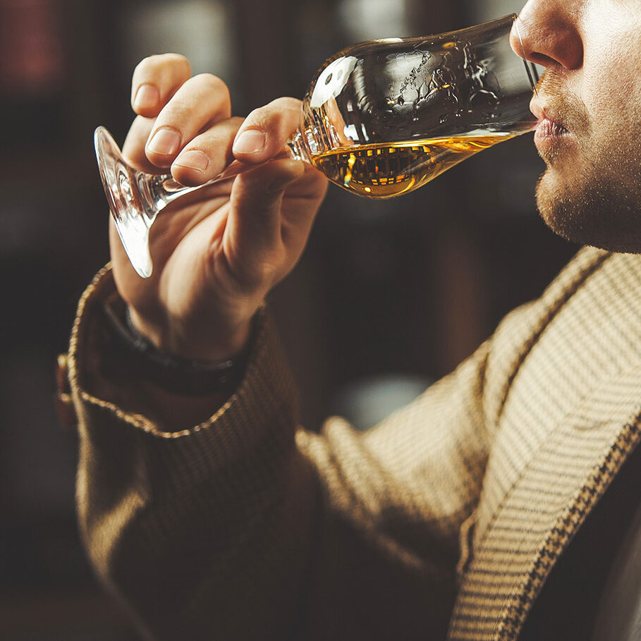 Close-up shot of sommelier tasting whiskey taste on the cellar background. Expert in the field of alcoholic beverages testing drink.