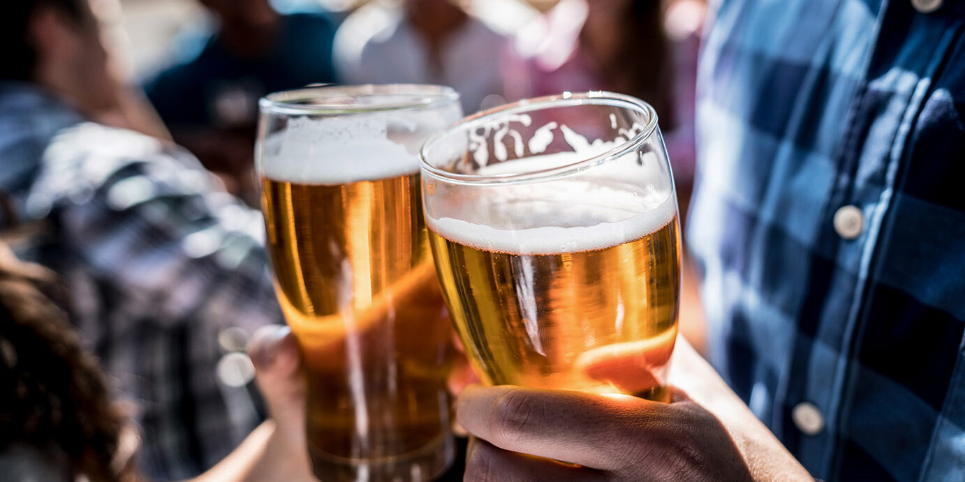 Close up of a customers at a bar holding a beer and making a toast Close up of a customers at a bar holding a beer and making a toast with people having fun at the background
