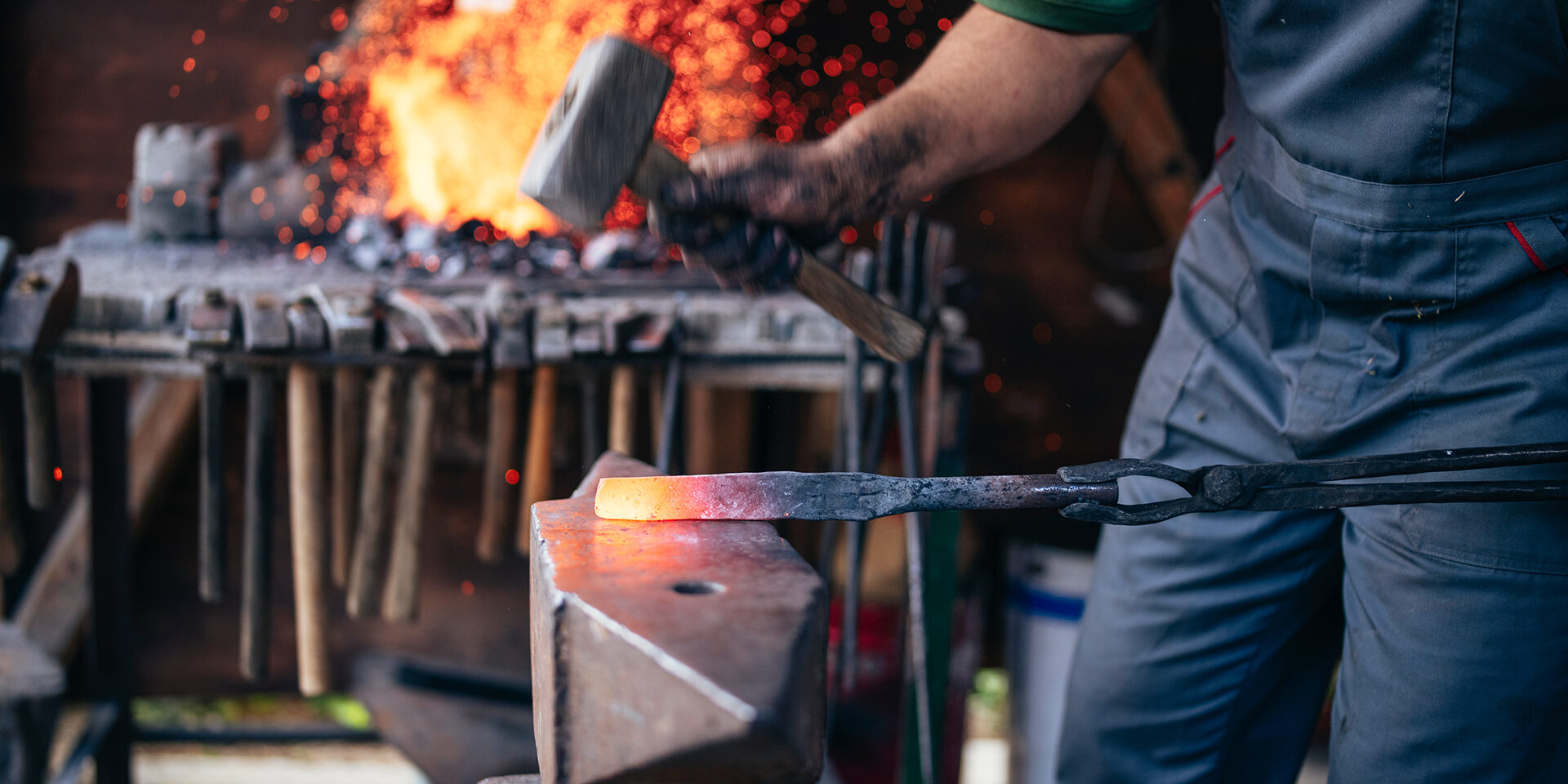 An unrecognizable blacksmith forges hot metal with a hammer on an anvile.
