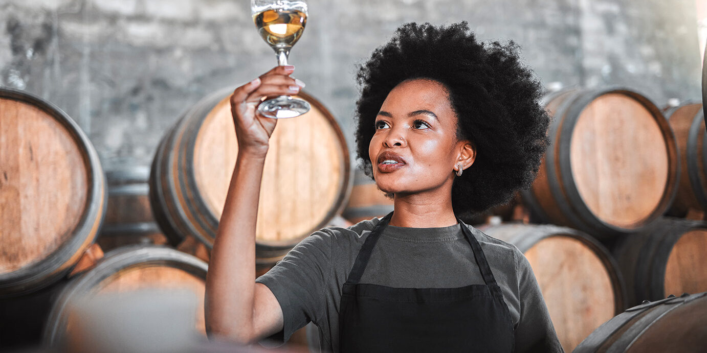 Black woman tasting wine at a winery, looking and checking the color and quality of the years produce. Young African American sommelier proud of the new addition, analyzing white wine in a cellar Black woman tasting wine at a winery, looking and checking the color and quality of the years produce. Young African American sommelier proud of the new addition, analyzing white wine in a cellar